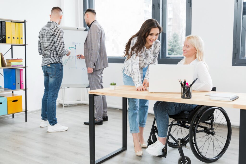 side-view-woman-wheelchair-conversing-with-female-coworker-office (1)